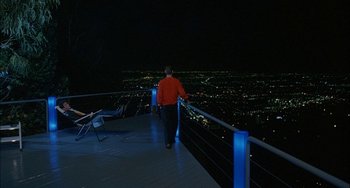 Movie still from “Less Than Zero” (1987), directed by Marek Kanievska – A man standing on a balcony at night looking at the city lights; Extreme Wide shot, High angle