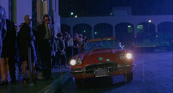 Movie still from “Less Than Zero” (1987), directed by Marek Kanievska – A man standing next to a red car on the street; Wide shot, Low angle