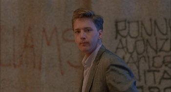 Movie still from “Less Than Zero” (1987), directed by Marek Kanievska – A man in a suit and tie standing in front of a wall; Close Up shot, Low angle