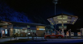Movie still from “Less Than Zero” (1987), directed by Marek Kanievska – A red car parked in front of a gas station at night; Extreme Wide shot, High angle