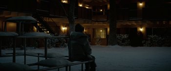 Movie still from “Let Me In” (2010), directed by Matt Reeves – A person sitting on a bench in front of a building at night; Wide shot, Over the shoulder angle