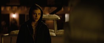 Movie still from “Let Me In” (2010), directed by Matt Reeves – A young woman wearing a hooded jacket standing in a dark room; Close Up shot, Over the shoulder angle