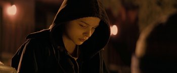 A young boy wearing a hooded jacket looking down