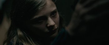 Movie still from “Let Me In” (2010), directed by Matt Reeves – A young girl looking into the camera with a dark background; Close Up shot, Over the shoulder angle