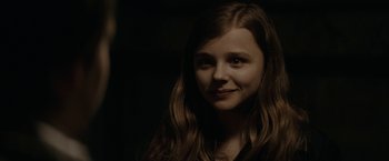 Movie still from “Let Me In” (2010), directed by Matt Reeves – A young girl with long brown hair smiles for the camera; Close Up shot, Over the shoulder angle