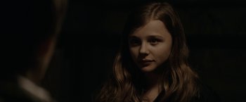 Movie still from “Let Me In” (2010), directed by Matt Reeves – A young girl with long brown hair is posing for the camera; Close Up shot, Over the shoulder angle