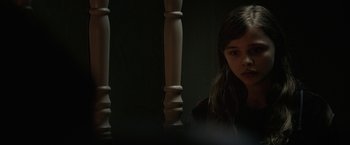 Movie still from “Let Me In” (2010), directed by Matt Reeves – A young girl sitting in front of wooden pillars; Close Up shot, Over the shoulder angle