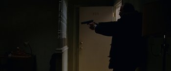 Movie still from “Let Me In” (2010), directed by Matt Reeves – A man holding a gun in front of a door; Medium shot, Low angle