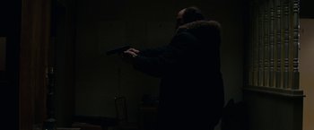 Movie still from “Let Me In” (2010), directed by Matt Reeves – A man holding a gun while standing in a room; Medium shot, High angle