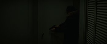 Movie still from “Let Me In” (2010), directed by Matt Reeves – A person holding a gun in a dark room; Medium shot, Over the shoulder angle