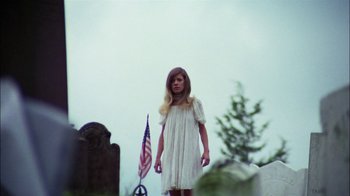Movie still from “Let's Scare Jessica to Death” (1971), directed by John D. Hancock – A woman in a white dress standing in front of a flag; Wide shot, Low angle