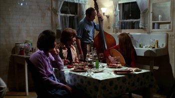 Movie still from “Let's Scare Jessica to Death” (1971), directed by John D. Hancock – A group of people sitting at a table with a guitar; Wide shot, High angle