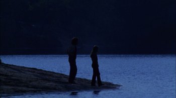 Movie still from “Let's Scare Jessica to Death” (1971), directed by John D. Hancock – Two people standing on the shore of a body of water at night; Wide shot, Low angle