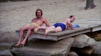Movie still from “Let's Scare Jessica to Death” (1971), directed by John D. Hancock – A couple of men sitting on top of a wooden dock; Wide shot, High angle