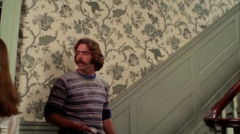 Movie still from “Let's Scare Jessica to Death” (1971), directed by John D. Hancock – A man standing in front of a floral wallpaper holding a nintendo wii controller; Medium shot, Low angle