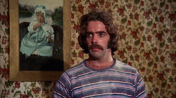 Movie still from “Let's Scare Jessica to Death” (1971), directed by John D. Hancock – A man in a striped t - shirt with a mustache looks to his left; Close Up shot, Over the shoulder angle