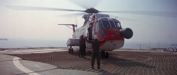 Movie still from “Leviathan” (1989), directed by George P. Cosmatos – Three people standing next to a red and white helicopter; Extreme Wide shot, High angle