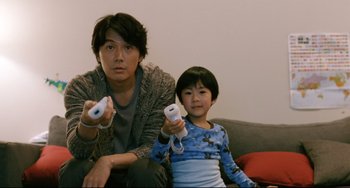 Movie still from “Like Father, Like Son” (2013), directed by Kore-eda Hirokazu – A man and a boy are holding wii remotes; Medium shot, Over the shoulder angle