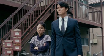 Movie still from “Like Father, Like Son” (2013), directed by Kore-eda Hirokazu – A man and a woman standing next to each other in front of a building; Medium shot, Low angle