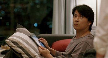 Movie still from “Like Father, Like Son” (2013), directed by Kore-eda Hirokazu – A man sitting on a couch looking at a tablet; Close Up shot, Over the shoulder angle