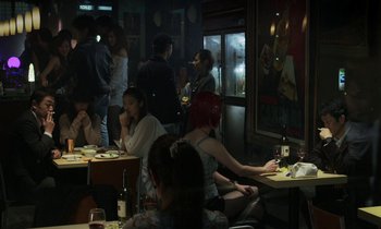 Movie still from “Like Someone in Love” (2012), directed by Abbas Kiarostami – A group of people sitting at tables in a room; Wide shot, Over the shoulder angle