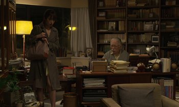 Movie still from “Like Someone in Love” (2012), directed by Abbas Kiarostami – An older man sitting at a desk in front of an older woman; Wide shot, Over the shoulder angle