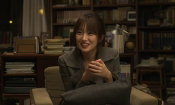 Movie still from “Like Someone in Love” (2012), directed by Abbas Kiarostami – A woman sitting in a chair in front of a bookshelf; Close Up shot, Over the shoulder angle