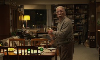 Movie still from “Like Someone in Love” (2012), directed by Abbas Kiarostami – An older man standing in front of a dining room table; Medium shot, Over the shoulder angle