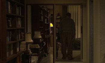Movie still from “Like Someone in Love” (2012), directed by Abbas Kiarostami – An older man standing in a living room at night; Wide shot, Over the shoulder angle