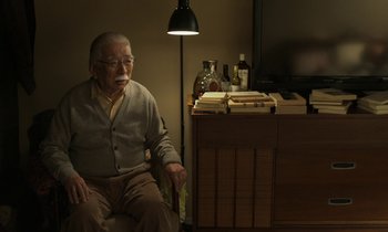 Movie still from “Like Someone in Love” (2012), directed by Abbas Kiarostami – An older man sitting in a chair in front of a desk; Medium shot, Over the shoulder angle