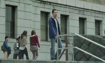 Movie still from “Like Someone in Love” (2012), directed by Abbas Kiarostami – A man standing on the side of a building next to a woman; Wide shot, Low angle