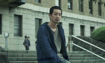 Movie still from “Like Someone in Love” (2012), directed by Abbas Kiarostami – A man sitting on the steps of a building; Medium shot, Low angle