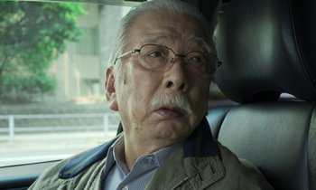 Movie still from “Like Someone in Love” (2012), directed by Abbas Kiarostami – An older man with glasses and a mustache in the back of a car; Close Up shot, Low angle