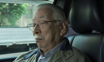 Movie still from “Like Someone in Love” (2012), directed by Abbas Kiarostami – An older man sitting in the back seat of a car; Close Up shot, High angle