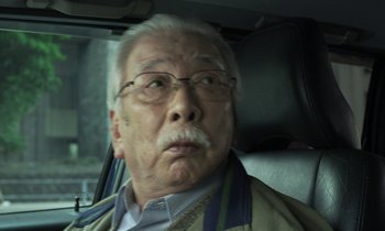 Movie still from “Like Someone in Love” (2012), directed by Abbas Kiarostami – An older man wearing glasses sitting in the back of a car; Close Up shot, Low angle