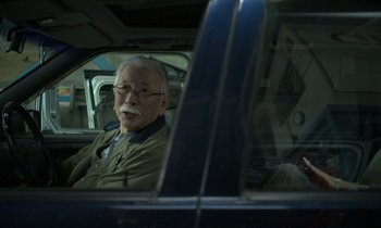 Movie still from “Like Someone in Love” (2012), directed by Abbas Kiarostami – An older man sitting in the back seat of a car; Medium shot, Over the shoulder angle