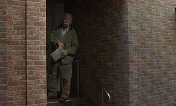 Movie still from “Like Someone in Love” (2012), directed by Abbas Kiarostami – An older man standing in front of a brick wall; Wide shot, Low angle