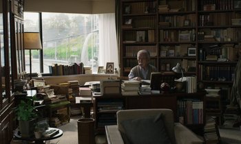 Movie still from “Like Someone in Love” (2012), directed by Abbas Kiarostami – An older man sitting in front of a computer in a room full of books; Wide shot, High angle