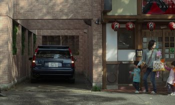 Movie still from “Like Someone in Love” (2012), directed by Abbas Kiarostami – A car parked in front of a brick building; Wide shot, Low angle