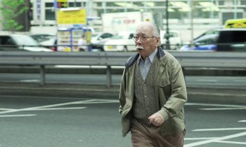 Movie still from “Like Someone in Love” (2012), directed by Abbas Kiarostami – An older man walking down the street with a cigarette in his mouth; Medium shot, Low angle