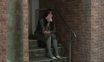 Movie still from “Like Someone in Love” (2012), directed by Abbas Kiarostami – A woman sitting on the steps holding a phone; Wide shot, Low angle