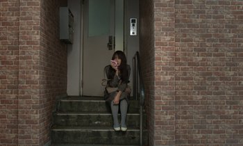 Movie still from “Like Someone in Love” (2012), directed by Abbas Kiarostami – A woman sitting on the steps of a building; Wide shot, High angle
