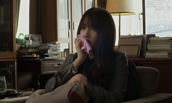 Movie still from “Like Someone in Love” (2012), directed by Abbas Kiarostami – A woman sitting in front of a window holding a pink cloth in front of her face; Medium shot, Over the shoulder angle