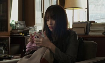 Movie still from “Like Someone in Love” (2012), directed by Abbas Kiarostami – A woman sitting on a couch holding a cell phone; Medium shot, High angle