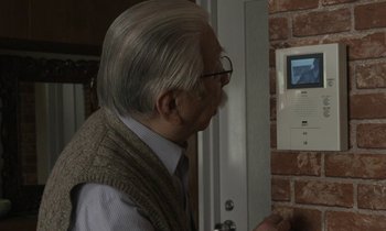 Movie still from “Like Someone in Love” (2012), directed by Abbas Kiarostami – An older man is looking at a video screen on the wall; Extreme Close Up shot, Low angle