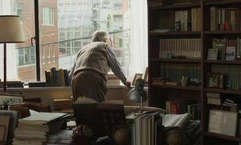Movie still from “Like Someone in Love” (2012), directed by Abbas Kiarostami – An older man standing in front of a large window; Medium shot, High angle