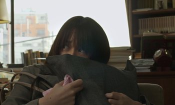 Movie still from “Like Someone in Love” (2012), directed by Abbas Kiarostami – A woman hiding her face behind a suit jacket; Medium shot, Over the shoulder angle