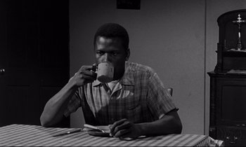 Movie still from “Lilies of the Field” (1963), directed by Ralph Nelson – A man sitting at a table drinking a cup of coffee; Medium shot, Low angle