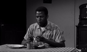 Movie still from “Lilies of the Field” (1963), directed by Ralph Nelson – A man sitting at a table with a cup of coffee; Medium shot, Low angle