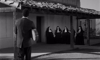 Movie still from “Lilies of the Field” (1963), directed by Ralph Nelson – A group of nuns sitting on a porch while a man plays a guitar; Wide shot, Over the shoulder angle